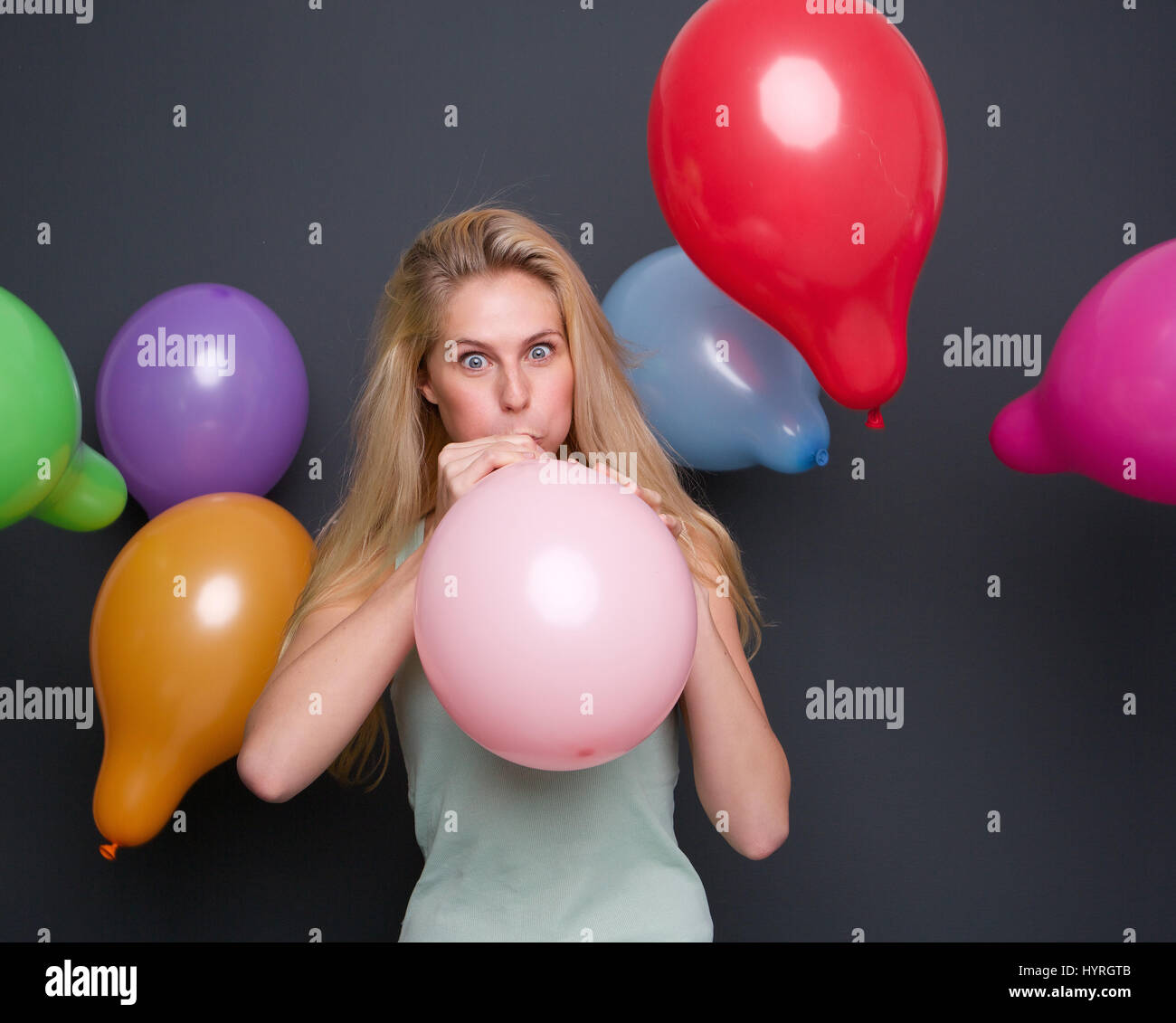 Portrait of a beautiful blond woman blowing up balloon on gray background Stock Photo