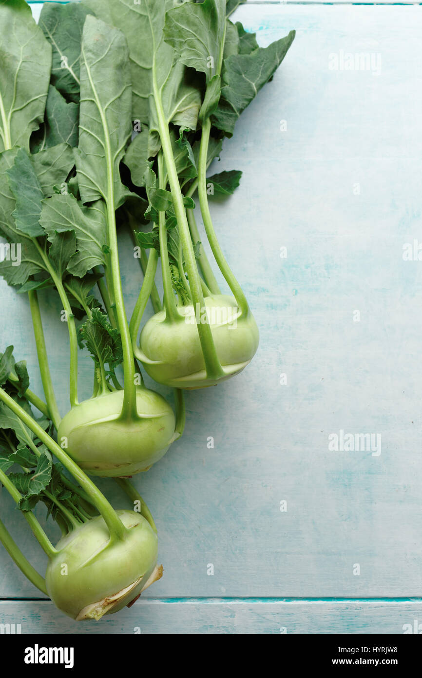 Fresh kohlrabi with green leaves. A bunch of freshly harvested kohlrabi on a blue table. Stock Photo