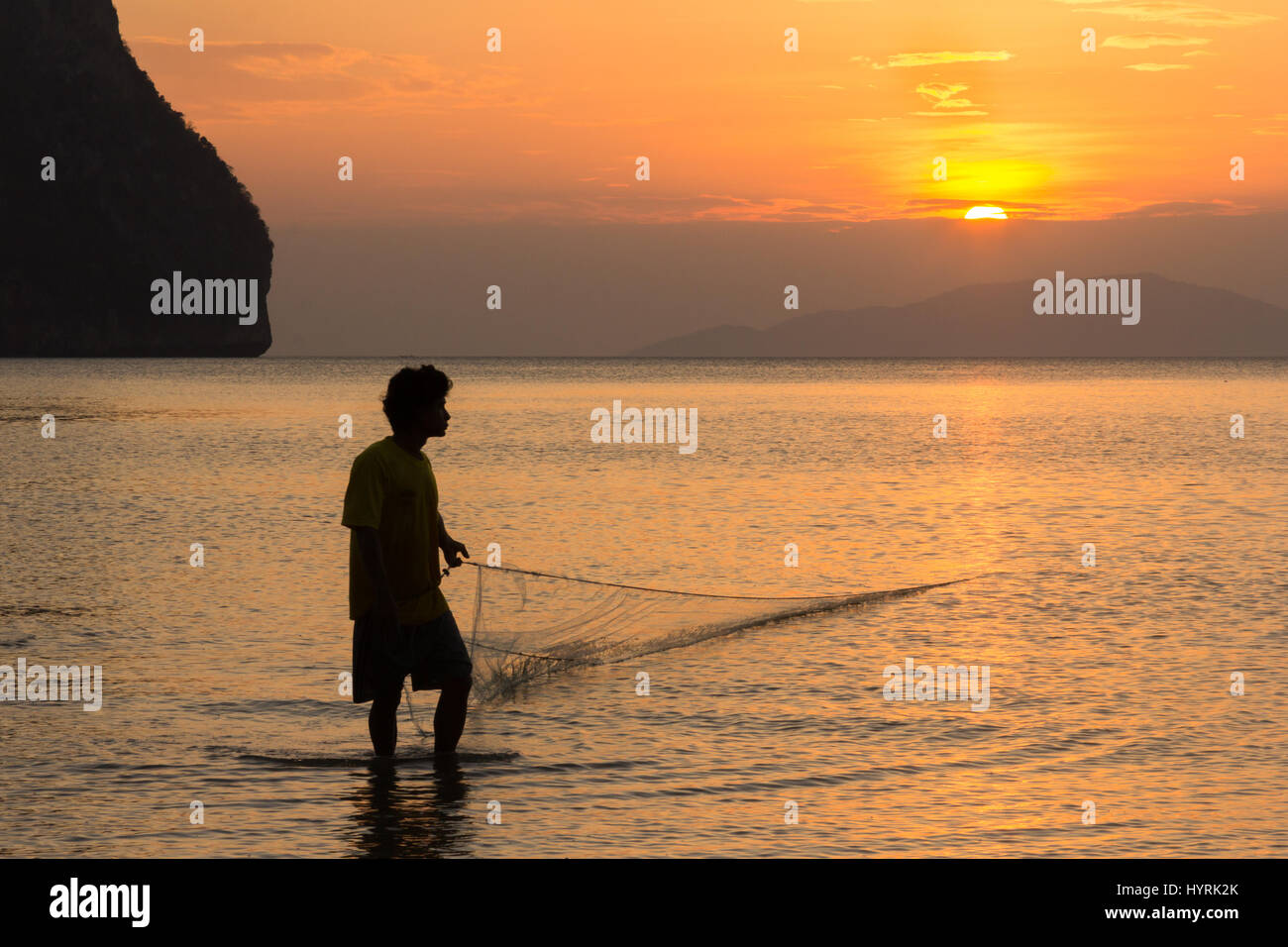 A fisherman pulls in his net at sunset on Rajamangala beach in Trang province, Thailand Stock Photo