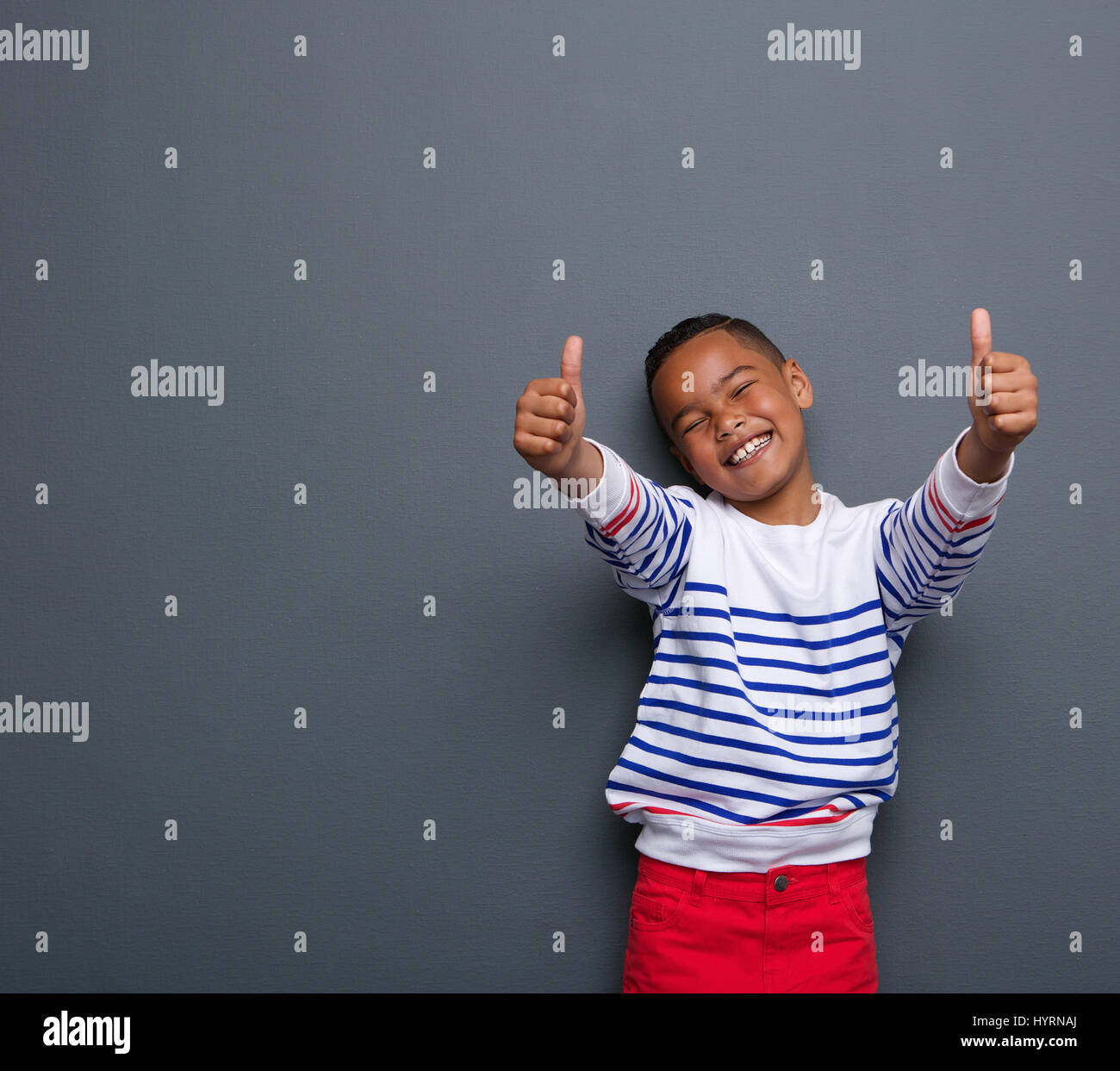 Portrait of a little boy laughing with thumbs up sign on gray ...