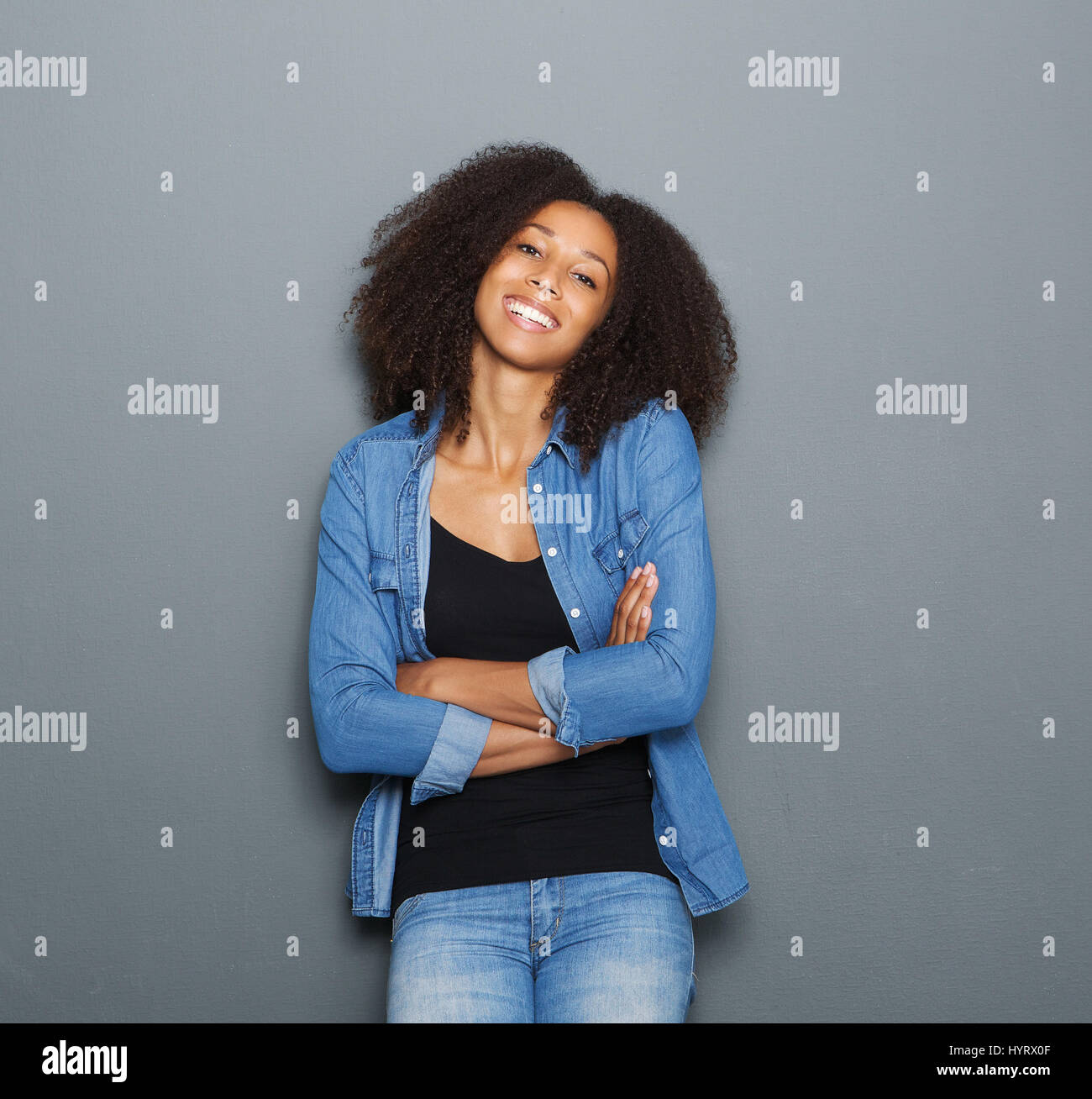 Portrait of a smiling young woman posing with arms crossed on gray ...