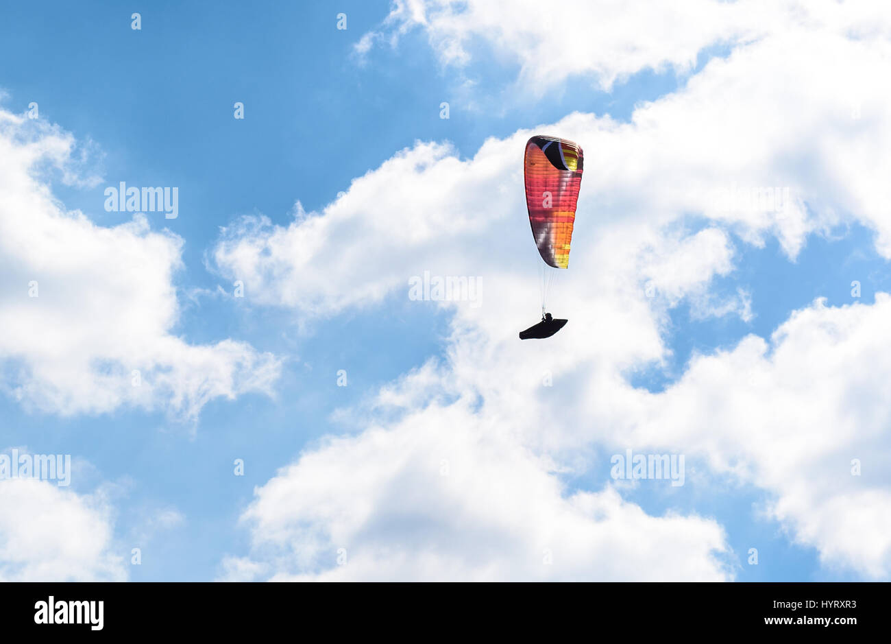 Paraglider flying against the blue sky with white clouds. Parachute on  a clear blue sunny day with sun and clouds. Stock Photo