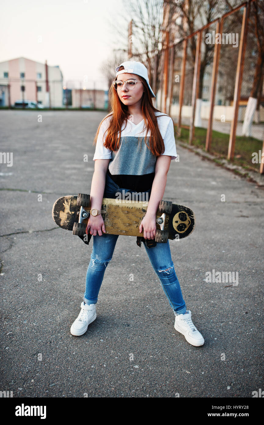 Young teenage urban girl with skateboard, wear on glasses, cap and ripped  jeans at the yard sports ground Stock Photo - Alamy