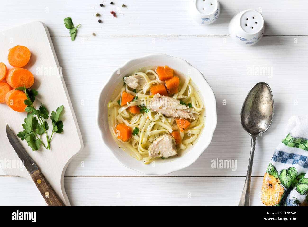 Fresh chicken soup with vegetables and pasta in a bowl with carrot and parsley on white table, top view Stock Photo