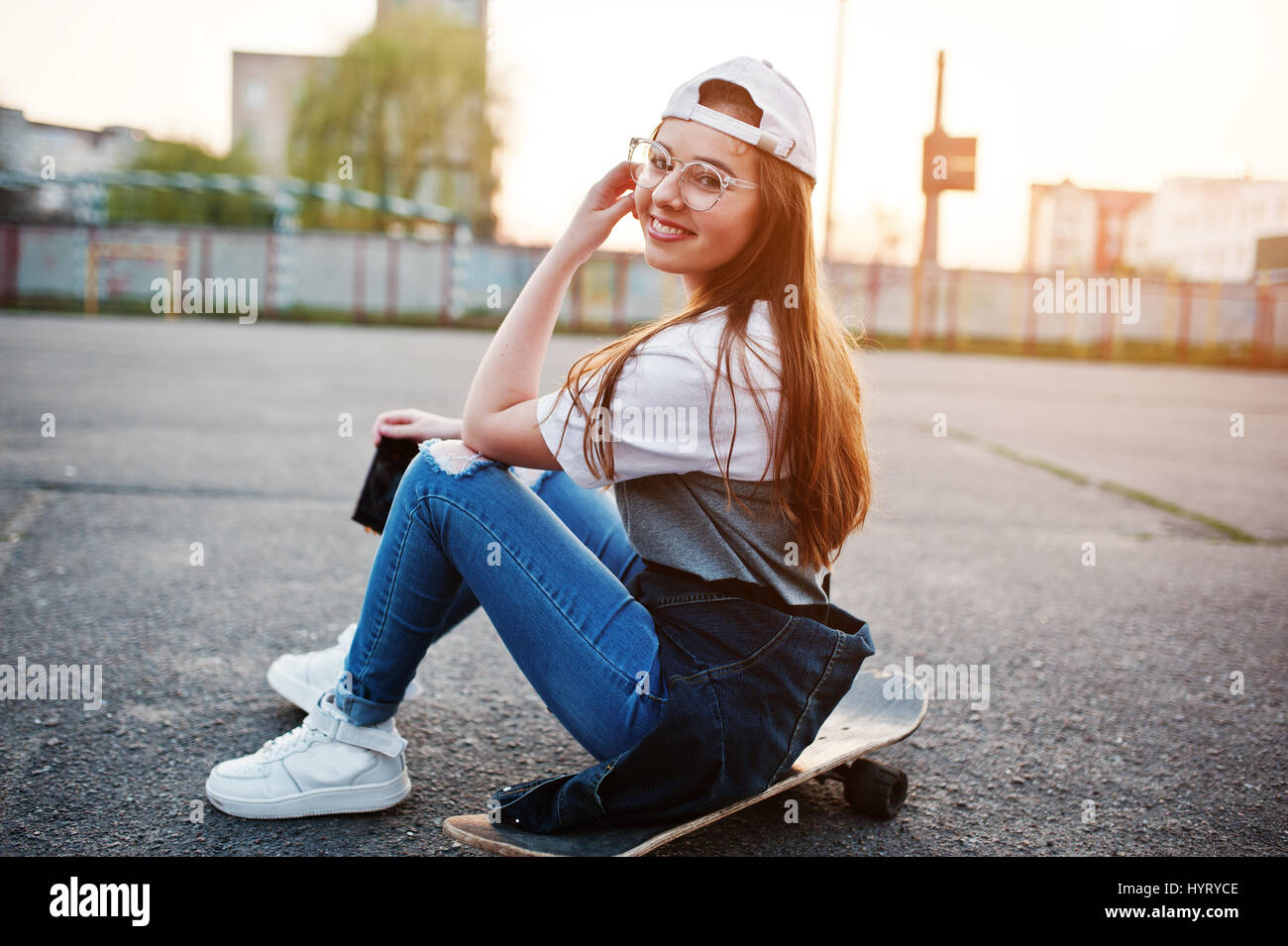 Young teenage urban girl with skateboard, wear on glasses, cap and ripped  jeans at the yard sports ground on sunset making selfie on phone Stock  Photo - Alamy