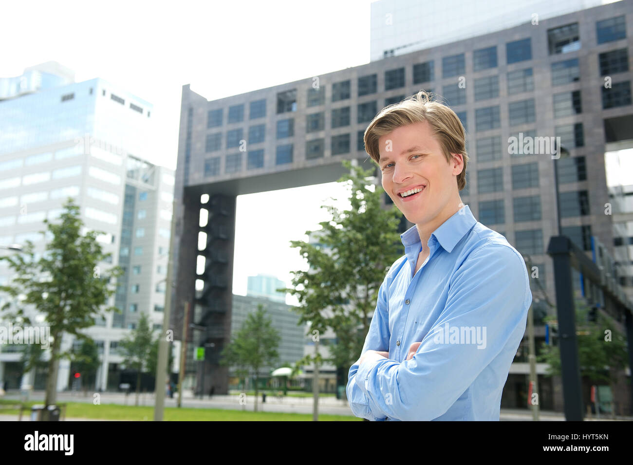 Smiling businessman posing with arms crossed outside city building ...