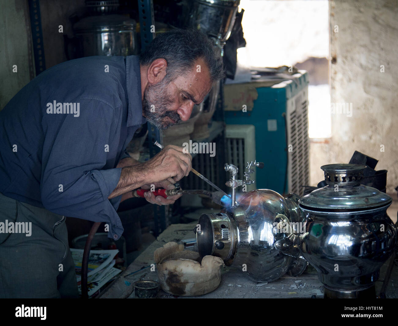 KASHAN, IRAN - AUGUST 13, 2016: Crafstman reparing a samovar in Kashan bazaar, Iran  Samovars (sometimes also spelled Samavar or Samaavar)  are used t Stock Photo