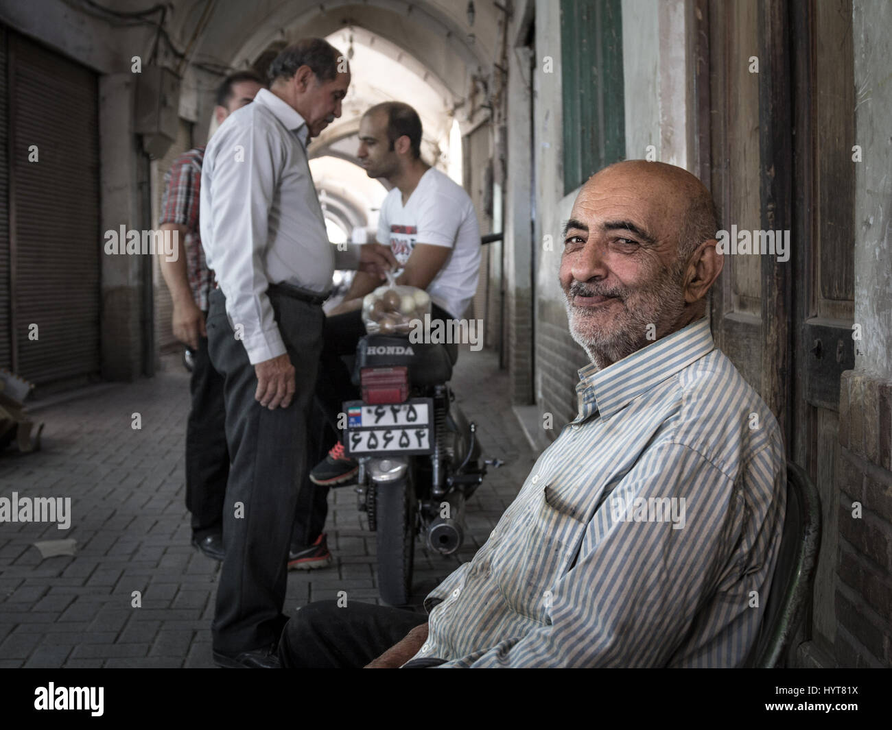 KASHAN, IRAN - AUGUST 13, 2016: Old Iranian egg seller smiling after a closing deal with fellow Iranian people in the background in Kashan Bazaar  Baz Stock Photo