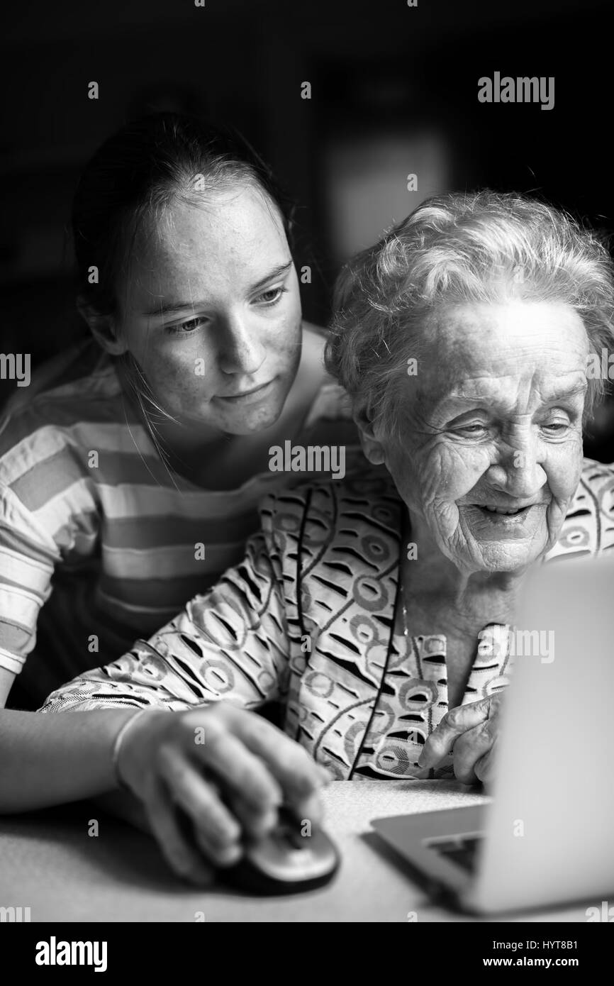 Girl teaches her grandmother to working on the computer. Black-and-white photo. Stock Photo