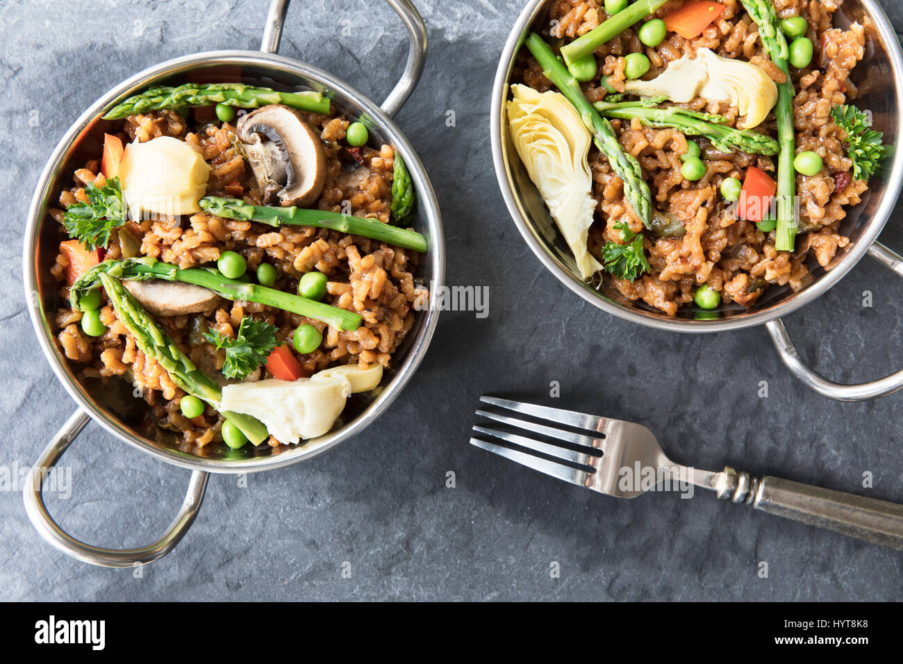 Two bowls of vegan paella with asparagus, mushrooms and artichoke