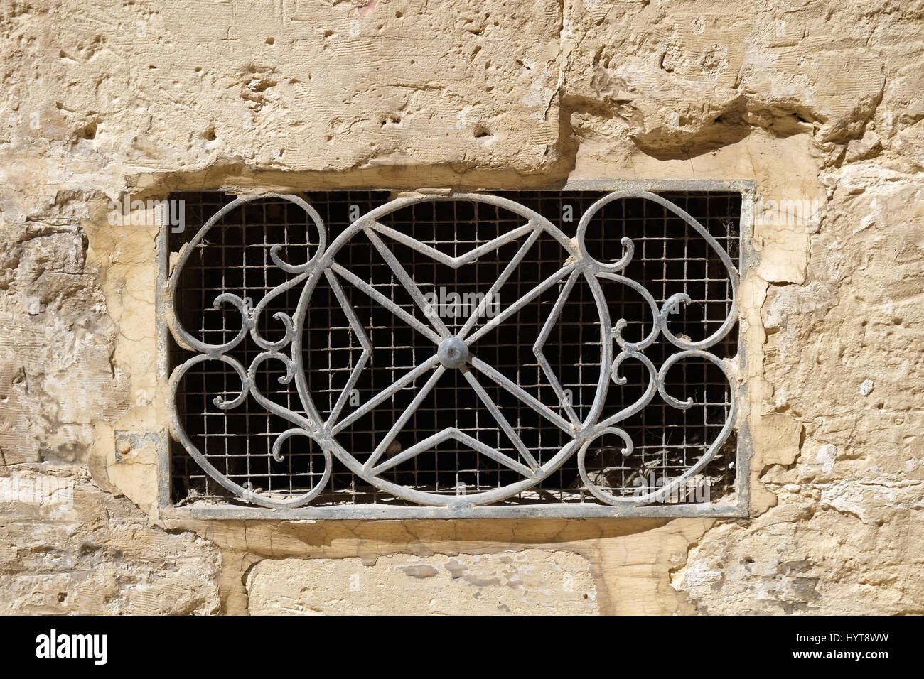 The decorative metal ventilation grill in form of 8-pointed Maltese cross  in a stone wall. Rabat. Malta Stock Photo - Alamy