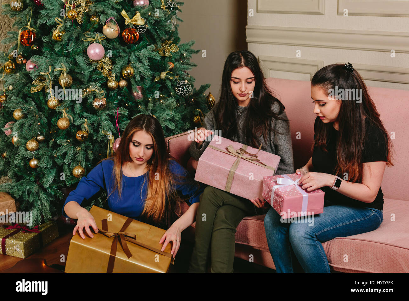 Three beautiful young girls unpack gifts near a Christmas tree. Studio horizontal portrait. Stock Photo