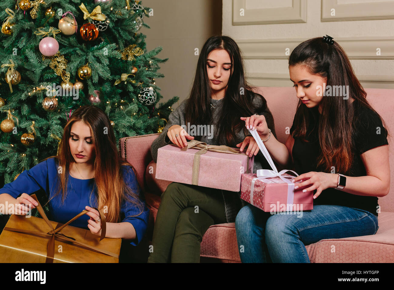 Three beautiful young girls unpack gifts near a Christmas tree. Studio horizontal portrait. Stock Photo