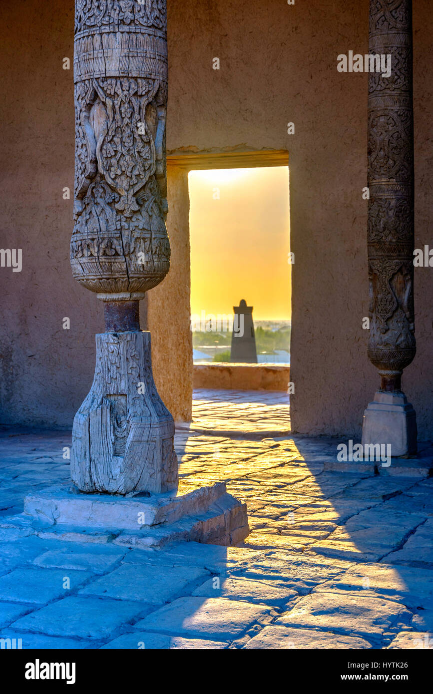 Old wooden pillars, and sun shining thru the door with the view to the minaret of Khiva old town, Uzbekistan Stock Photo