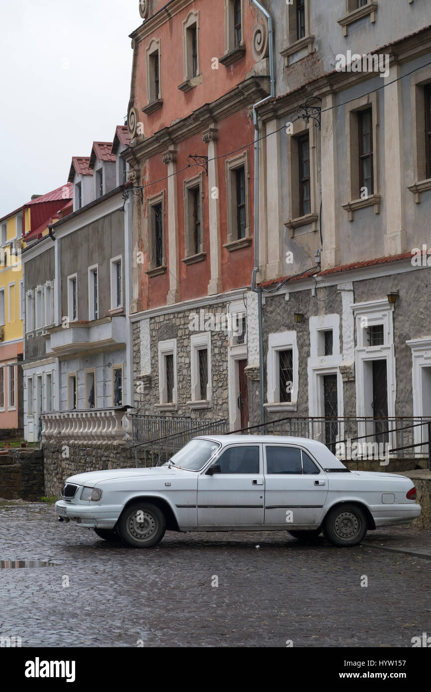 Old white Volga car parked on a cobbled side street in Kamianets-Podilskyi, Western Ukraine. The street is still wet from recent rains Stock Photo