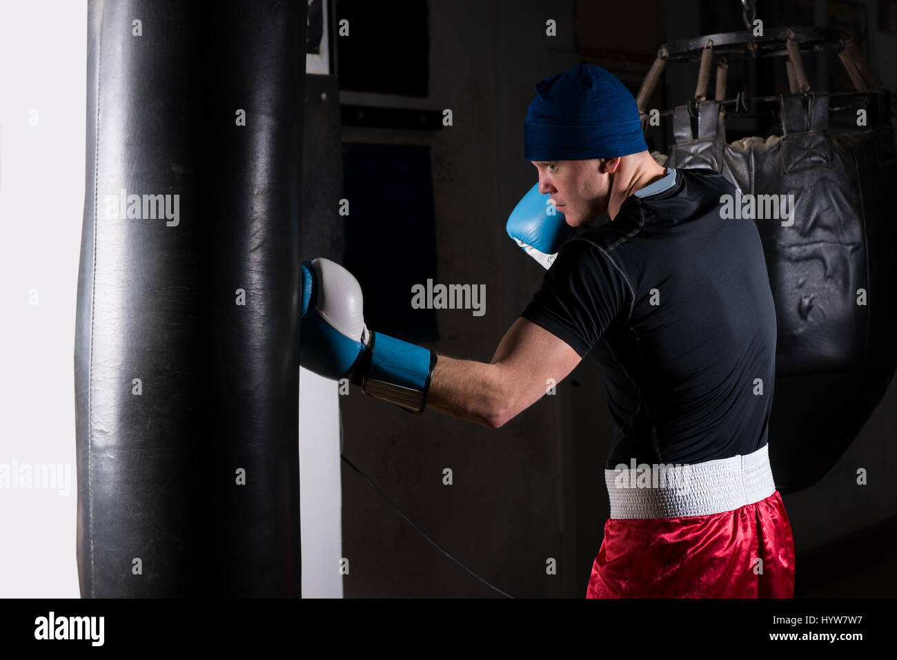 Young sporty man in boxing gloves training with boxing punching bag in