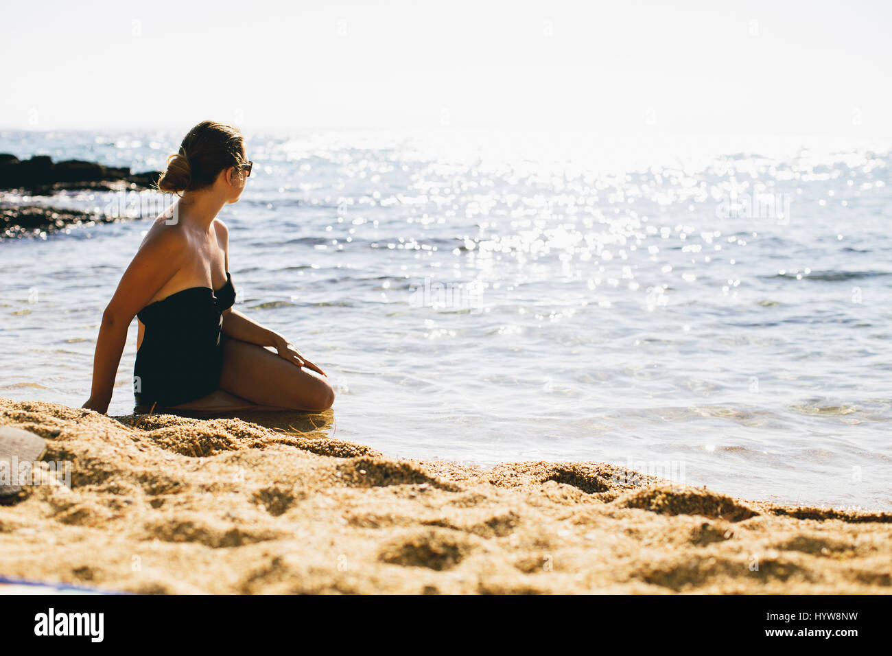Young women in bathing suit sitting in the sand by the sea Stock Photo