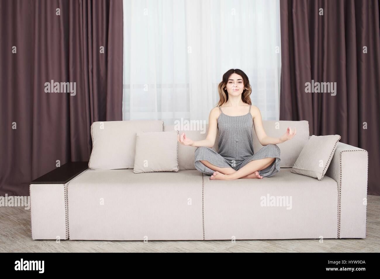 Young woman sitting on a sofa in the lotus position meditating Stock Photo