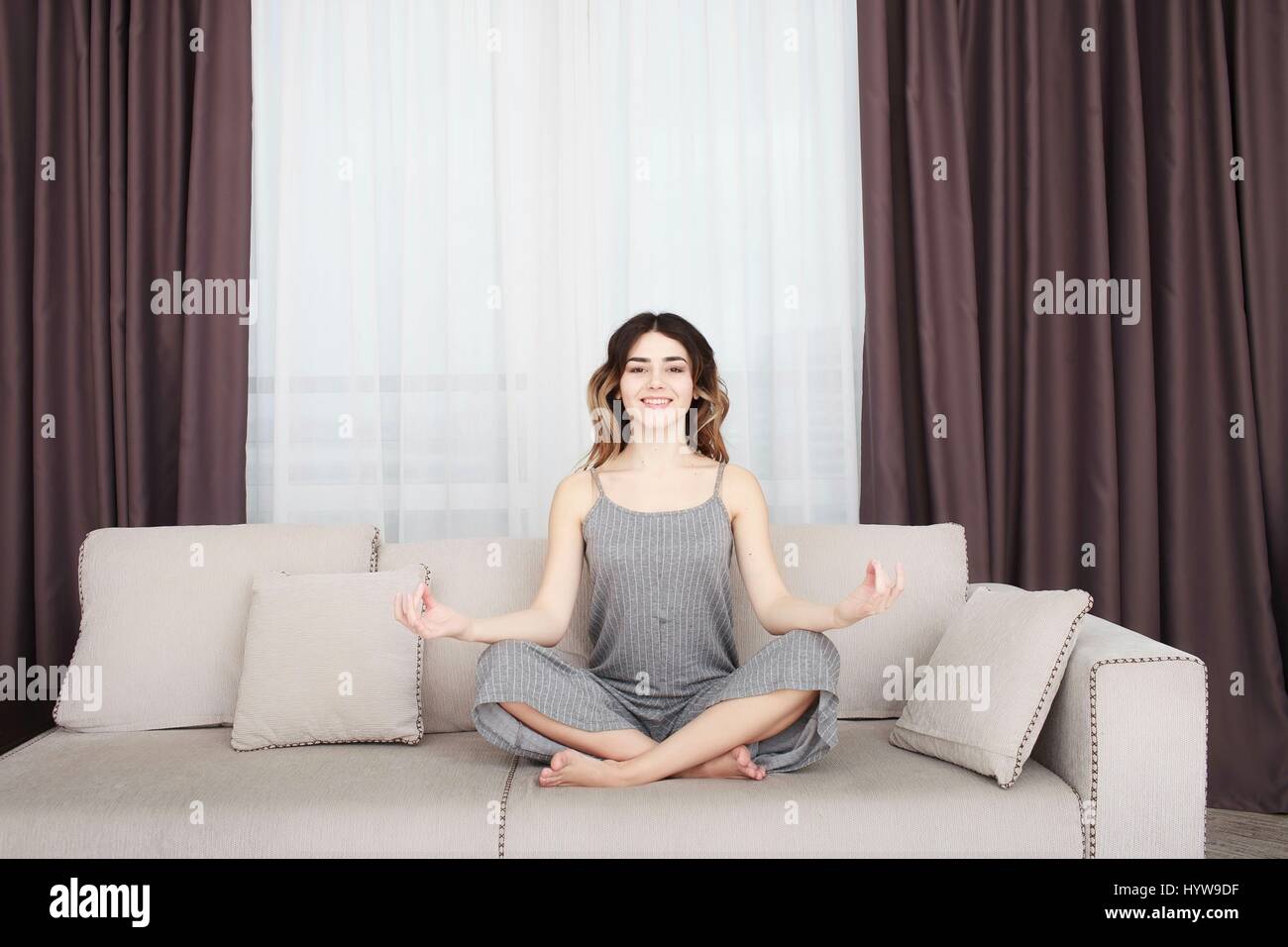 Young woman sitting on a sofa in the lotus position meditating Stock ...