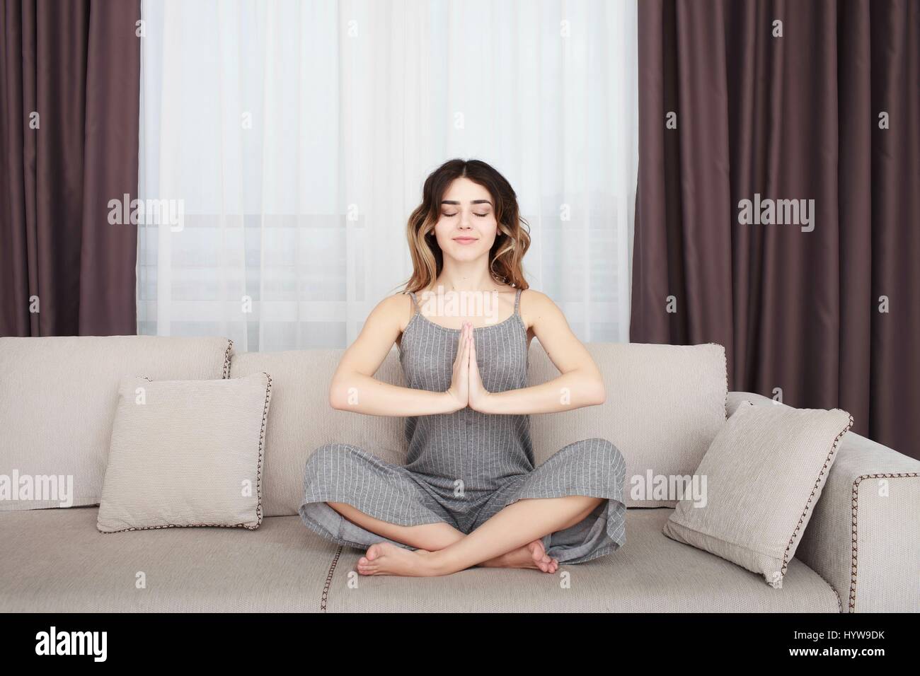 Young woman sitting on a sofa in the lotus position meditating Stock Photo