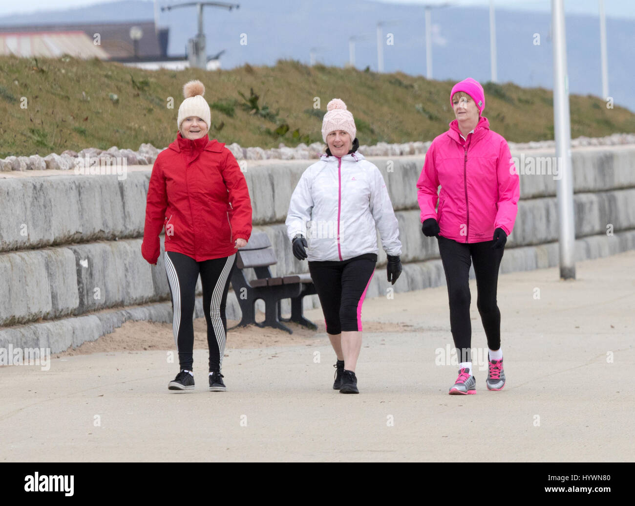 Three female friends walking along the Wales Coastal Path along Rhyl Promenade on a chilly morning getting some excercise, Denbighshire, Wales, UK Stock Photo