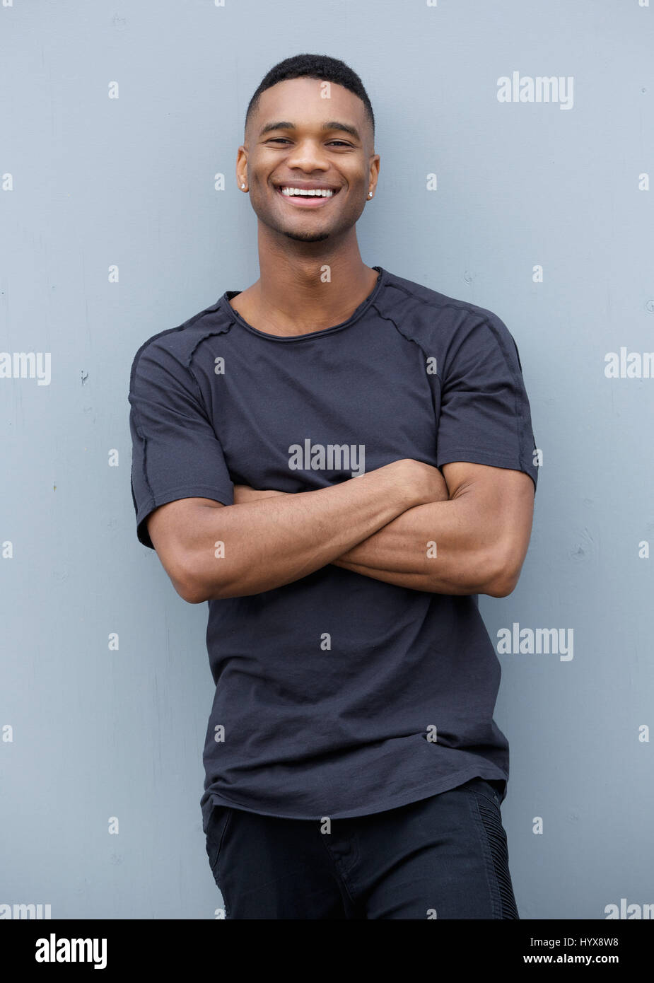 Portrait of a friendly black man smiling with arms crossed against gray ...