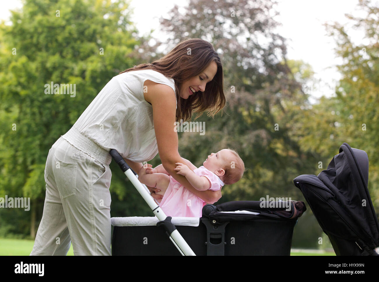 Side view portrait of a mother putting baby into pram Stock Photo