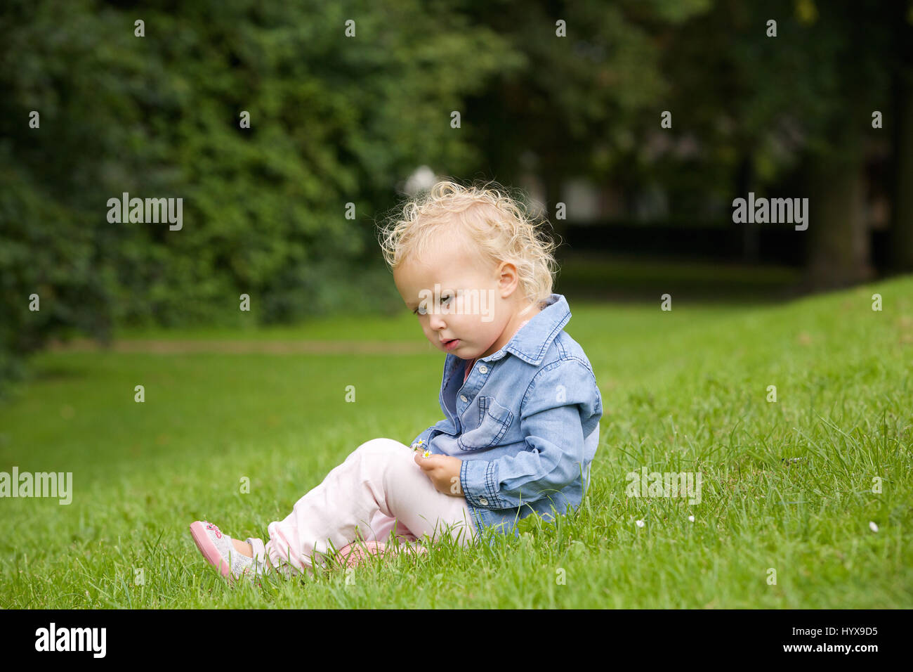 Portrait of a cute little girl sitting on green grass outdoors Stock ...