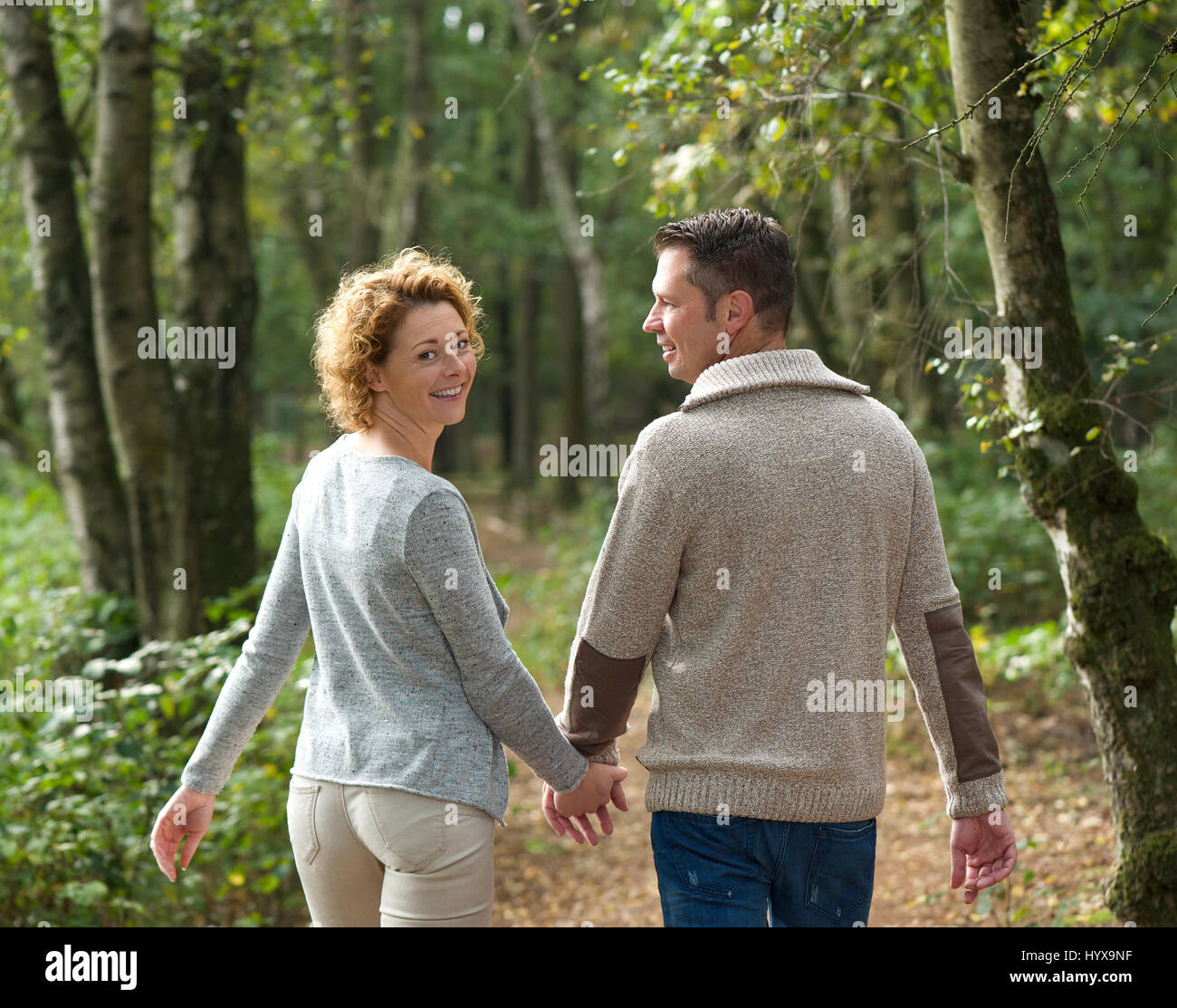 Portrait of a happy couple holding hands and walking in the forest Stock Photo