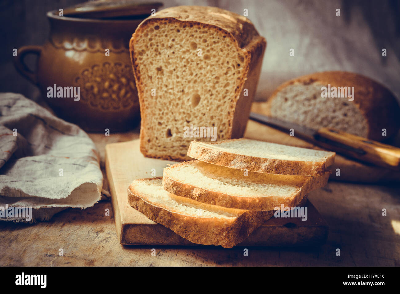 Sourdough bread loaf, sliced on old wood cutting board, vintage crockery, linen towel, authentic rural style, still life, toned Stock Photo