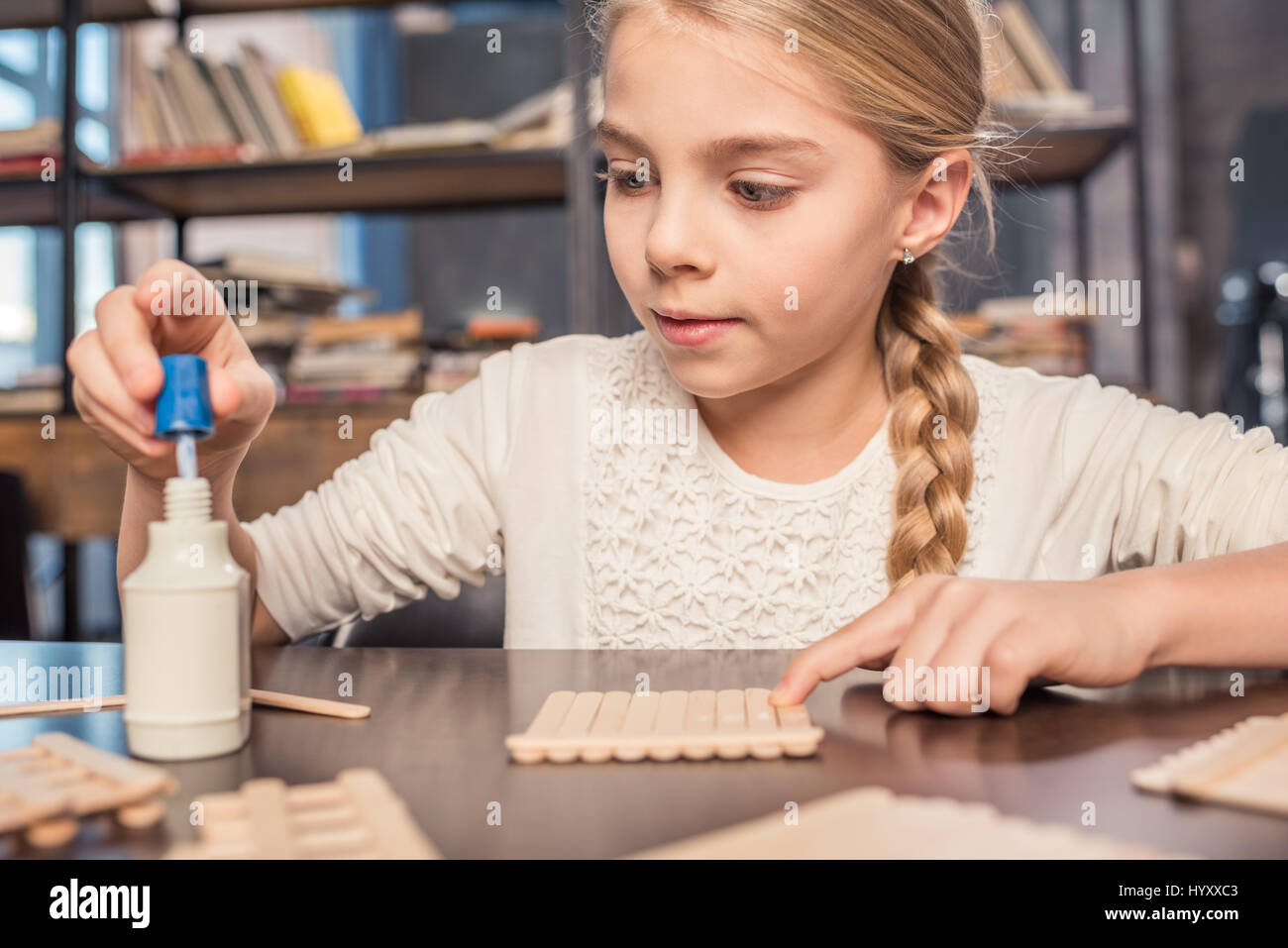 Concentrated little girl handcrafting with ice cream sticks and glue