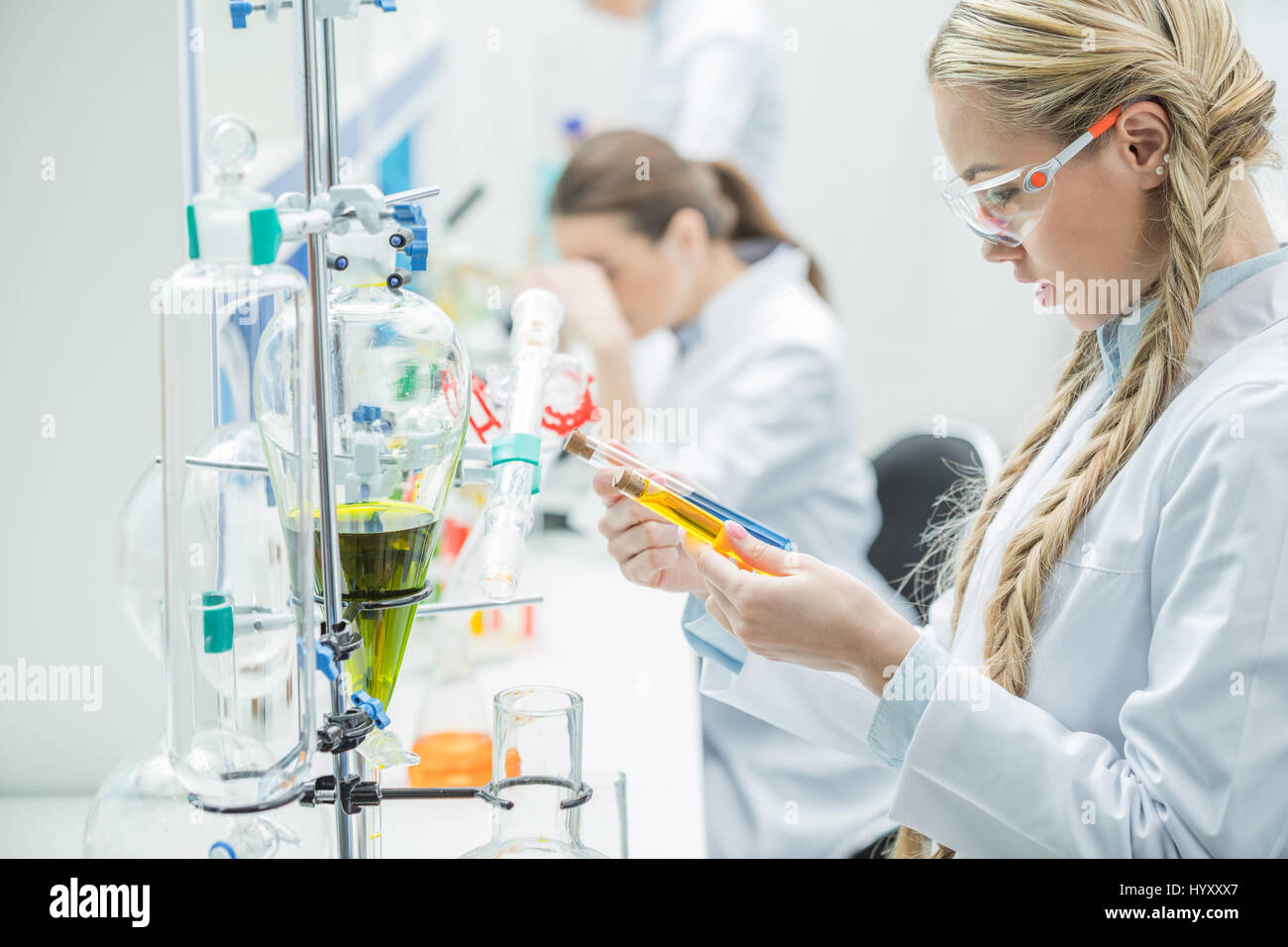 Young female scientist in protective glasses and lab coat looking at