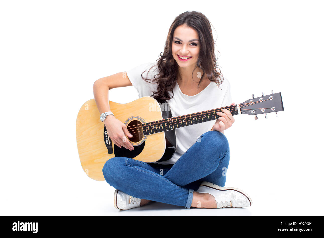 Smiling young woman sitting and playing guitar isolated on white Stock Photo