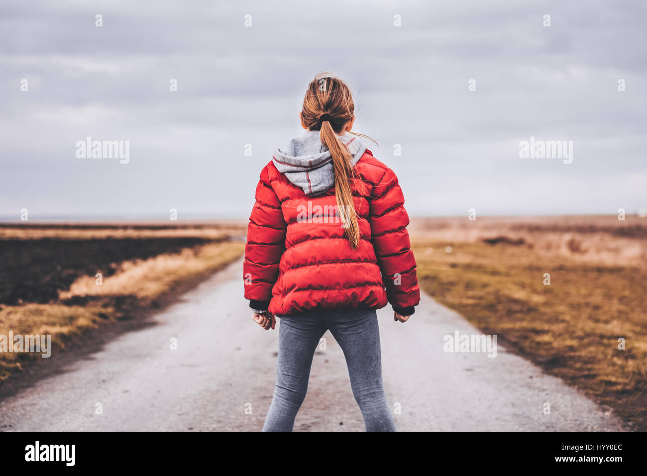 Girl wearing red jacket standing alone on the road and looking at distance Stock Photo