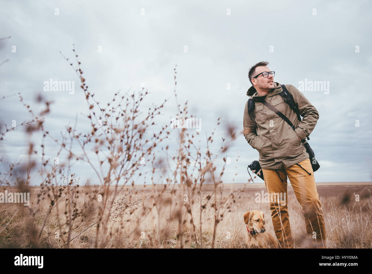 Hiker and dog walking in high grass on a cloudy day Stock Photo