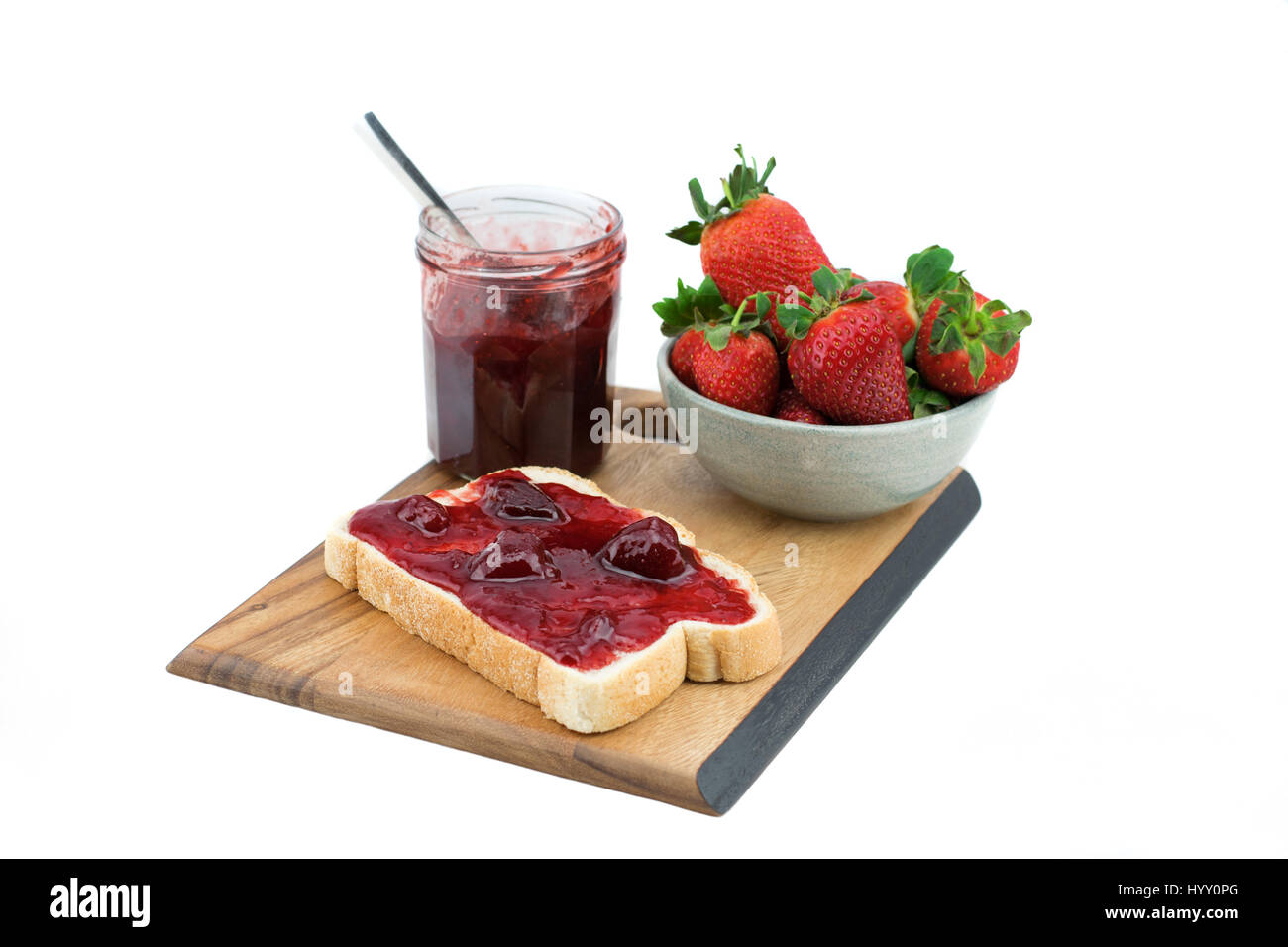 Bread with strawberry jam on a wooden board. Tasty breakfast. Ripe strawberries isolated on white background. Stock Photo