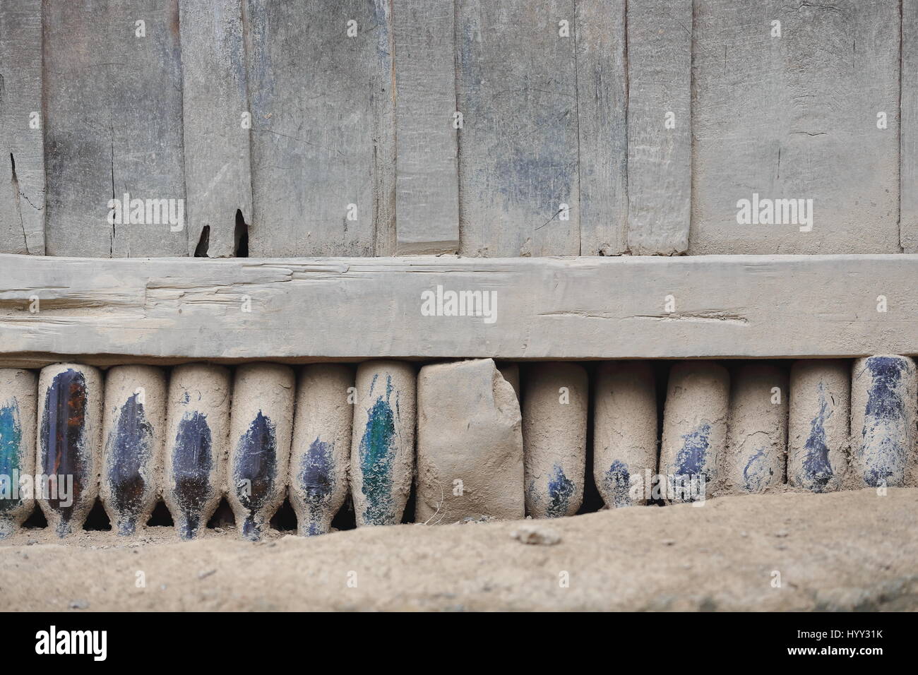 Foundation of uprightly placed empty beer bottles sustaining the wooden wall of a cottage in a village of the Akha Pala hill tribe in the Pak Nam Noy  Stock Photo