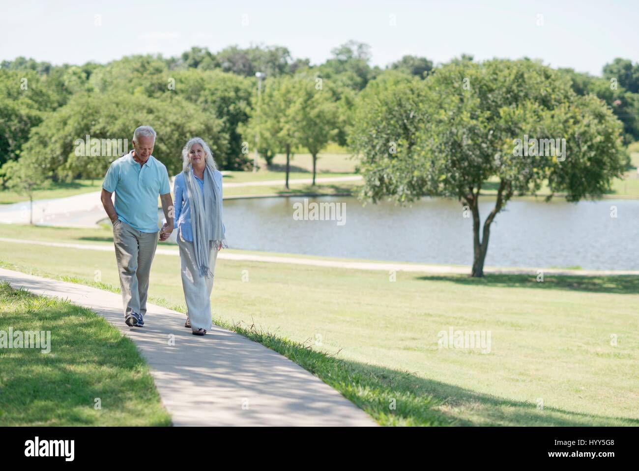 Senior couple walking on path in park by lake. Stock Photo