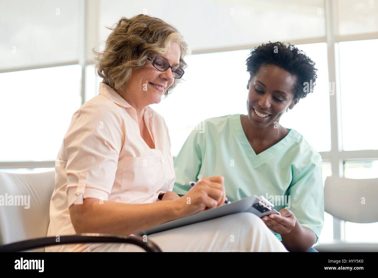 Mature woman filling out form with nurse, smiling. Stock Photo