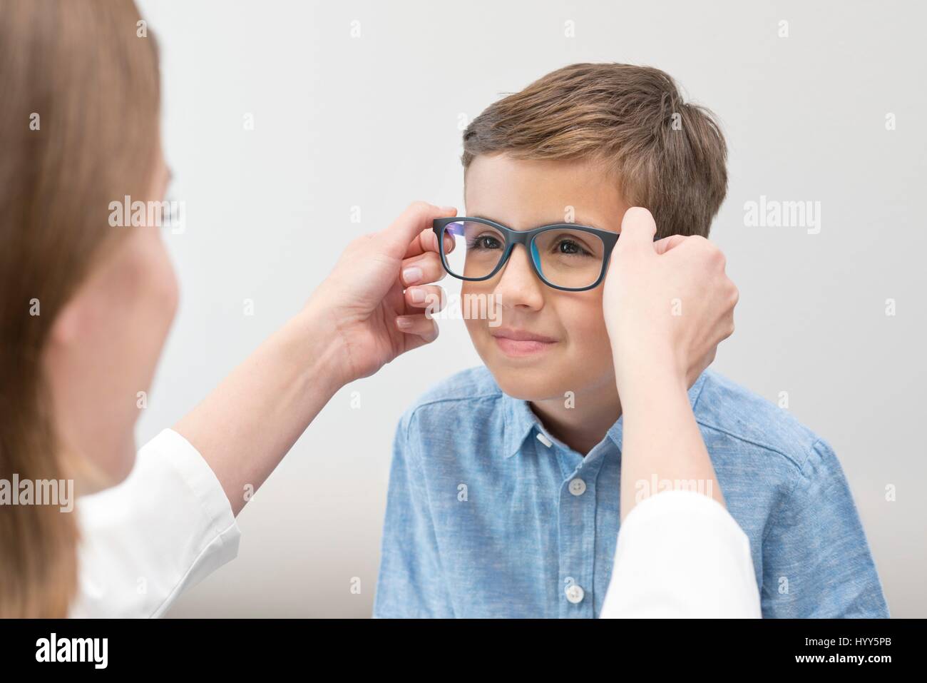 Female optician putting glasses on boy. Stock Photo