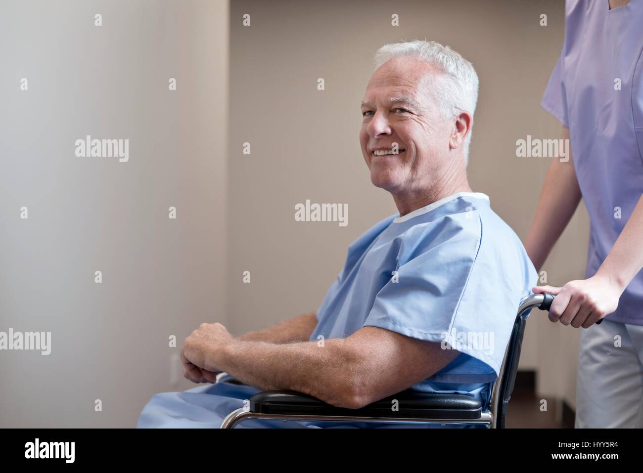 Senior man in hospital gown in wheelchair, smiling. Stock Photo
