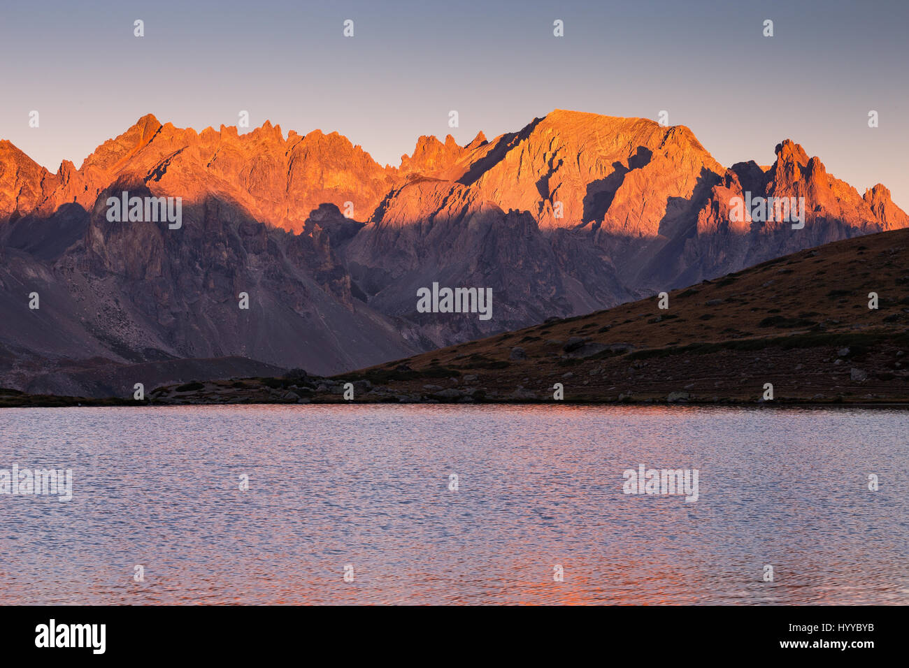 View from lake Laramon. Reddish color at dawn on mountain peaks of the Vallée de la Clarée. Névache. Hautes Alpes. France. Europe. Stock Photo