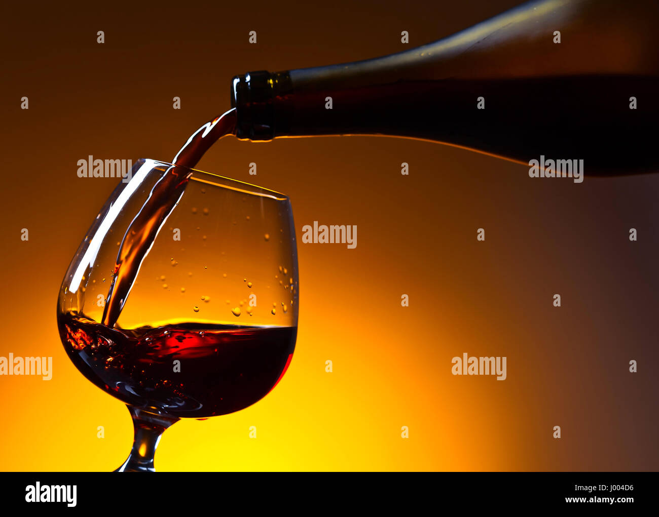 Brandy poured into a glass on a yellow background . Bottle and snifter