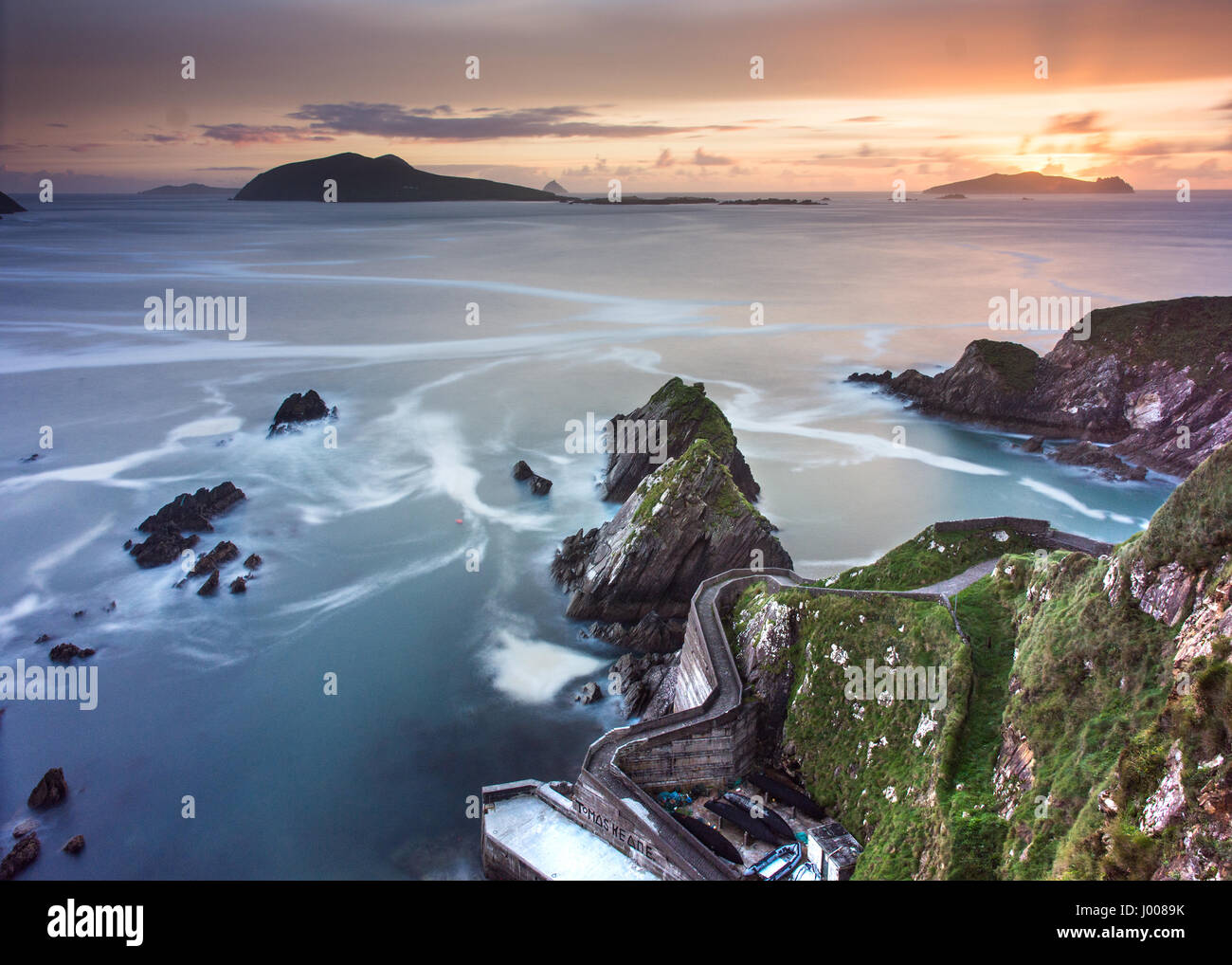 A narrow winding path leads down steep cliffs to Dunquin Pier, with the Blasket Islands beyond, on the rocky Atlantic Coast of the Dingle Peninsula in Stock Photo