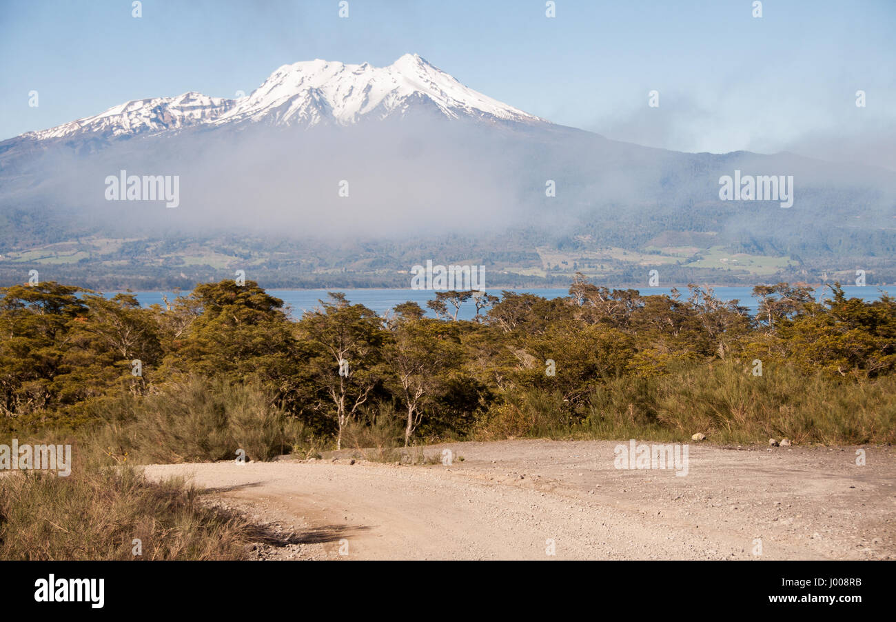 Mist rises from woodland on the shores of Lago Llanquihue, partially obscuring the snow-capped volcano of Calbuco in the Los Lagos region of Chilean P Stock Photo