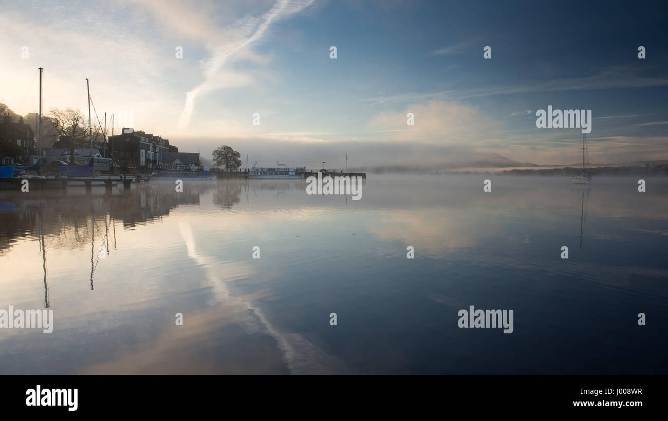 Mist rises from the calm waters of Windermere lake at Waterhead Pier, beside Ambleside Youth Hostel, in England's Lake District National Park. Stock Photo
