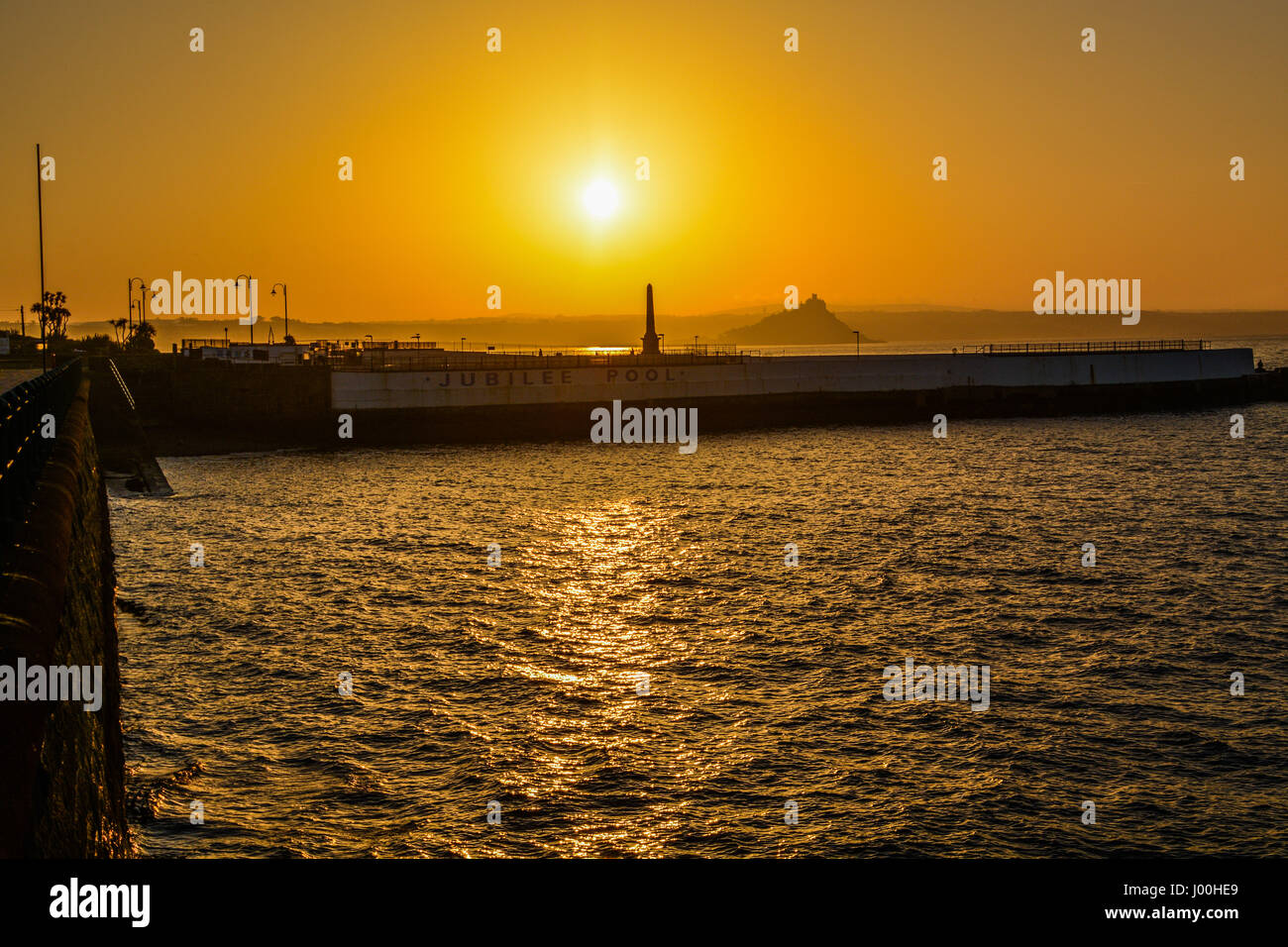 Penzance, Cornwall, UK. 8th Apr, 2017. UK Weather. The sun rises over Mounts Bay, and the Jubilee Pool - the outdoor Lido swimming pool, which has been closed for more refurbishment. Early morning haze lngered on the horizon, bringing a vivid orange glow around the sun. Credit: Simon Maycock/Alamy Live News Stock Photo