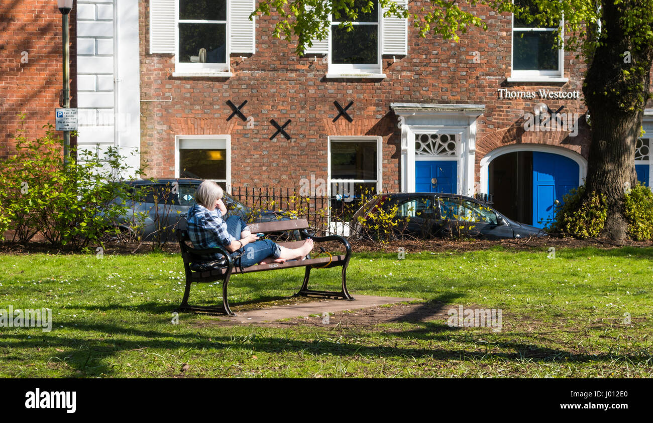 Blonde female sitting in a park in the commercial district of Exeter city centre,centre, using a mobile phone. Stock Photo