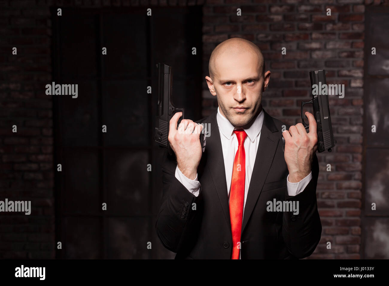Contract killer wallpaper, background or poster concept. Assassin in suit and red tie holding pistols in hand Stock Photo