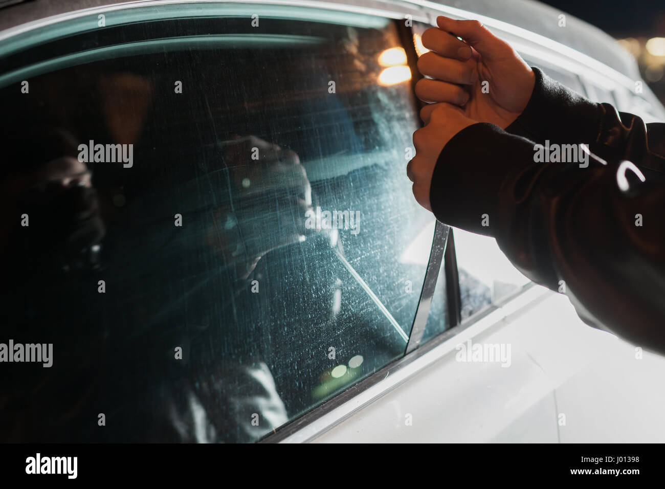 Male carjacker with balaclava on his head trying to open car door with ruler. Thief unlock vehicle. Auto transport insurance marketing Stock Photo